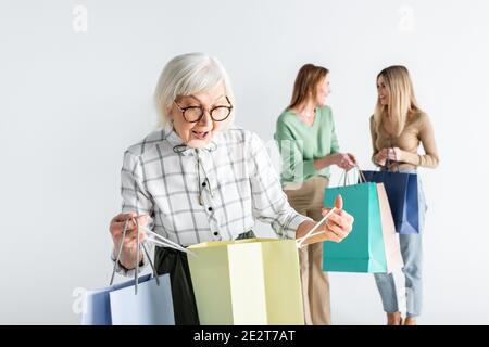 surprised senior woman looking at shopping bag near daughter and granddaughter on blurred background Stock Photo