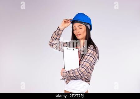 A young engineer straightens his blue helmet and holds a folder in his hands. White background. Gender non-lethality. Stock Photo