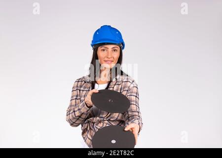 Young brunette in hard hat posing with abrasive discs on a white background. The concept of gender stereotypes. Stock Photo