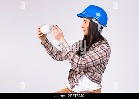An electrician woman examines a LED lamp in her hands on a white background. The concept of gender stereotypes. Stock Photo
