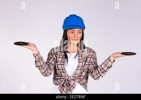 A woman in a hard hat with outstretched arms looks to the side and holds abrasive disks on a white background. Stock Photo
