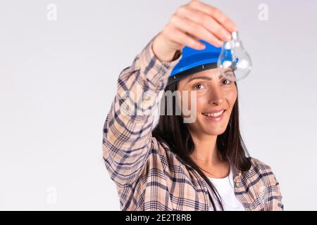 Young brunette in hard hat posing with light bulb and smiling on white background with side space. Stock Photo