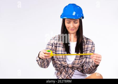 Handywoman with a smile in a blue hard hat with a tape measure on a gray background with empty space for advertising. Stock Photo