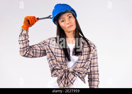 Portrait of a mechanic woman in a hard hat with a key looking at the camera on a white background. Stock Photo