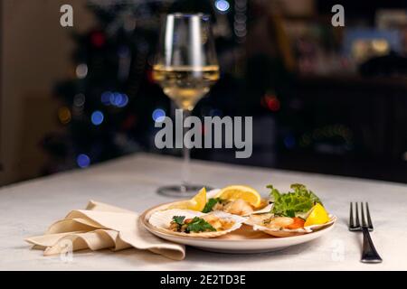 Baked scallops with caviar in a plate against the background of blurred glasses of wine. Scallops with lemon on a black background with a napkin and a Stock Photo