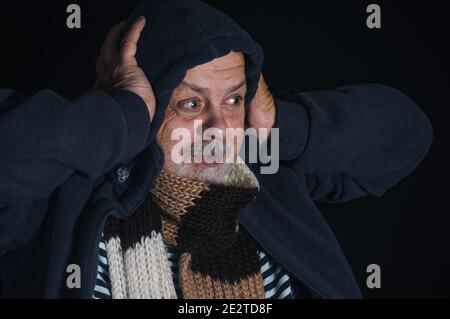 Nice low key portrait of smiling Caucasian senior man wrapping himself in warm clothes Stock Photo