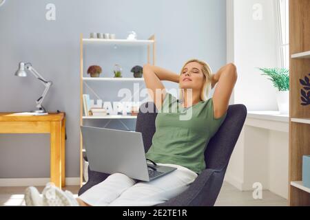 Woman relaxing in an armchair with computer on lap, feeling satisfied after finishing work Stock Photo