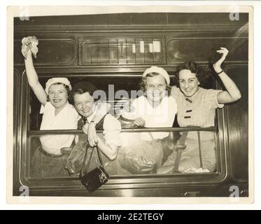 WW2 era press photo of happy young female walkers at train station, waving from a steam train window, London, U.K., 1940's Stock Photo