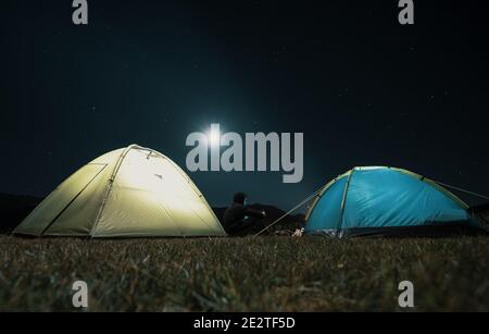 Camping in the mountains under the moon. A tent pitched up and glowing under the sky. Stock Photo