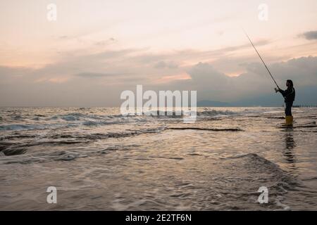 Fisherman in action. He stands in water and holds fly rod in one hand and  spoon in the other one. Also adult has a fishing net on the back. Green  Stock Photo - Alamy