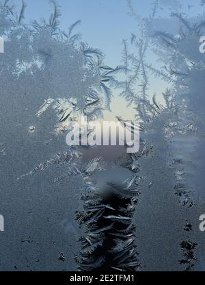 Frost pattern on window with glimpse of sunset outdoor behind crystals Stock Photo