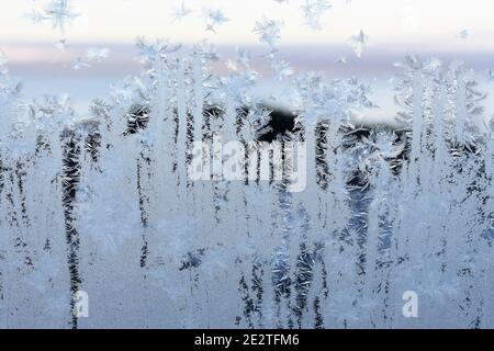 Frost pattern on window with glimpse of sunset outdoor behind crystals Stock Photo