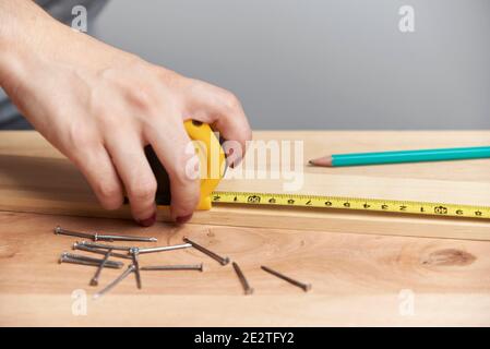 Detail of a young woman working in carpentry, using a measuring tape to make measurements on a wood strip. Stock Photo