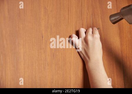 Young woman driving a nail into a wooden surface using a hammer. Closeup image with copy space. Stock Photo