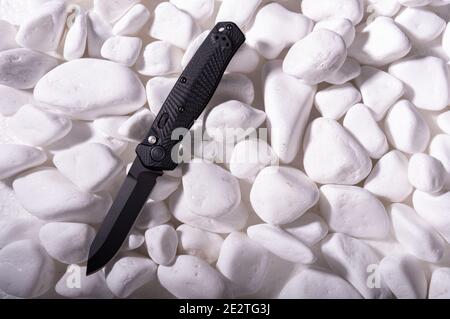 Black pocket knife on white stones. Black knife on a white background. Stock Photo