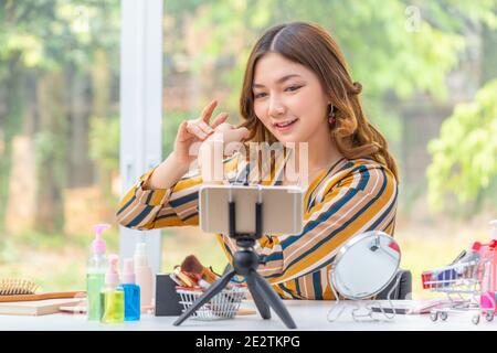 Happy beautiful young Asian woman, vlogger,  reviewing beauty products through her online video blog from her home Stock Photo