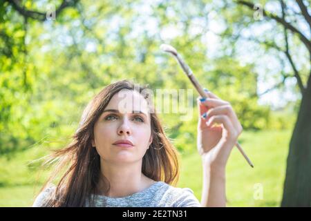 Portrait of a young woman looking upwards holding a paint brush on bright green background Stock Photo