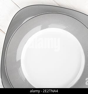 White round classical porcelain plates with a gray pattern stand on a white wooden table Stock Photo