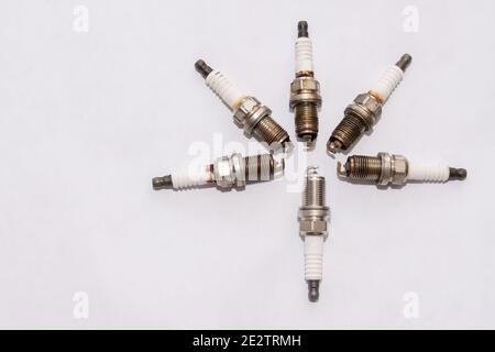 a set of old worn out petrol car spark plugs lie next to one new one on a blank clean white background Stock Photo