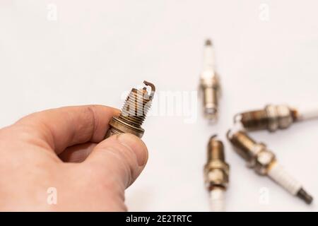 a man's hand holds an old worn out gasoline car spark plug on an empty clean white background Stock Photo