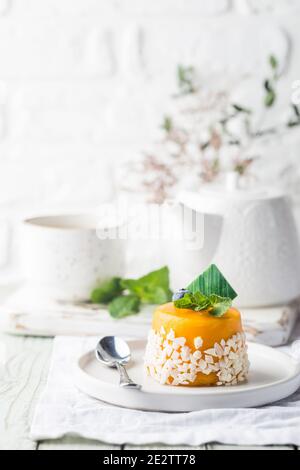 Piece of mango mousse cake on plate over white wooden table. Stock Photo