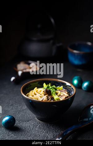 Asian ramen noodles soup with beef, oyster mushrooms and vegetables in bowl on dark background Stock Photo