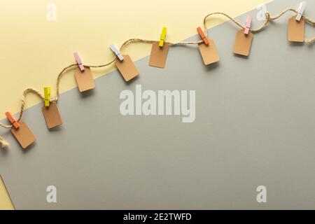Paper tags tied with colored clothespins to jute rope, rope with tags on trendy yellow gray background Stock Photo