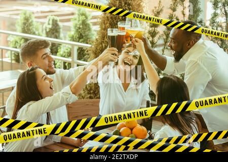 Group of friends clinking glasses with beer bounding tapes Lockdown, Coronavirus, Quarantine, Warning - closing bars, restaurants and nightclubs during pandemic. Lowed social life, ban of group meeting. Stock Photo