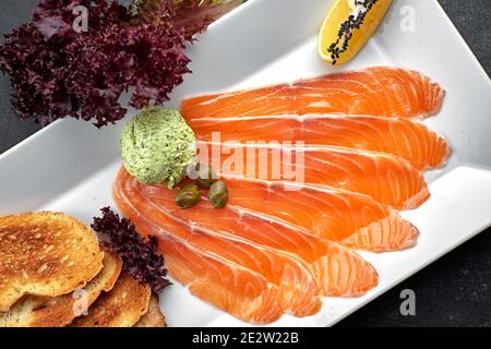 Salmon carpaccio, on a white platter, with croutons and lemon Stock Photo