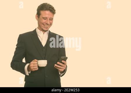 Happy Caucasian businessman using mobile phone while holding coffee cup Stock Photo