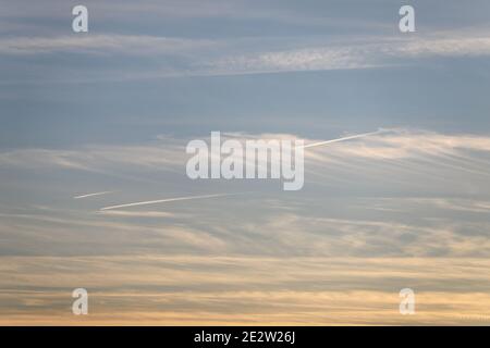 White and yellow clouds float across the blue sky, feather clouds, the sun is nearing sunset. Stock Photo