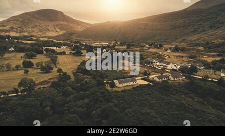 Sunset over mountain at village aerial. Nobody nature landscape at sun set. Cottages, houses at road. Whiskey distillery at valley. Cinematic Loch-Ranza, Arran island, Scotland, United Kingdom, Europe Stock Photo