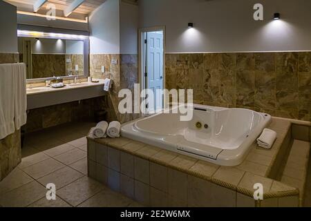 A marble-tiled bathroom with a large whirlpool bathtub and a double vanity belongs to a room near Lance aux Epines, Grenada – probably at the Calabash Hotel. Rolled white towels are laid out at the edge of the tub. Stock Photo
