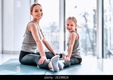 Happy healthy family in yoga center. Joyful mother and happy daughter doing stretching exercise on yoga mats near panoramic windows Stock Photo