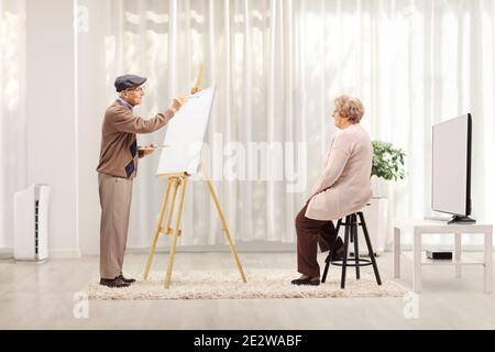 Elderly man painting a portrait of an elderly female model on a canvas in a room Stock Photo