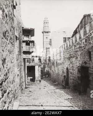 Vintage 19th century photograph: The Via Dolorosa is a processional route in the Old City of Jerusalem, believed to be the path that Jesus walked on the way to his crucifixion. The winding route from the former Antonia Fortress to the Church of the Holy Sepulchre — a distance of about 600 metres — is a celebrated place of Christian pilgrimage. Stock Photo