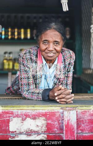 Ranohira, Madagascar - April 29, 2019: Unknown Malagasy woman shopkeeper leaning at table, smiling, in her market stall on the street. People of Madag Stock Photo