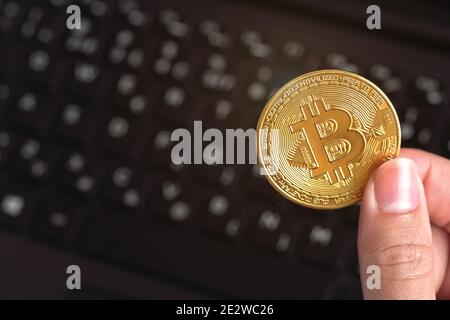 Woman hand holding golden coloured bitcoin coin over black laptop keyboard Stock Photo