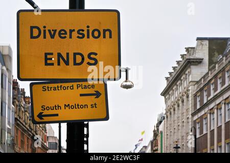 Yellow and black Diversion Ends sign with arrows pointing to Stratford Place and South Molton street, blurred building in background Stock Photo