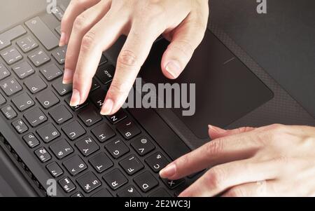 Woman hands typing on black laptop keyboard, close up detail from above Stock Photo