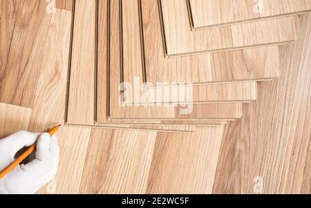 Installing laminated floor, detail on man hand with white glove holding red pencil, making mark on wooden tile Stock Photo