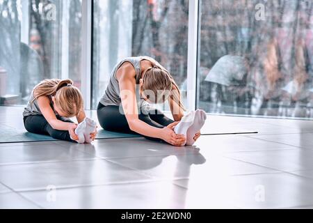 Sporty mother and daughter. Front view of athletic young woman and her little daughter in sportswear doing stretching before training sitting on the m Stock Photo