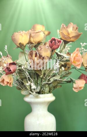 A flower white vase with a bouquet of autumn brown colored artificial roses on green background with vintage tone. Stock Photo