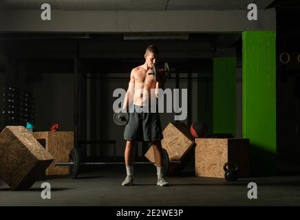 Young bodybuilder training dumbbell alternate biceps curl in home gym Stock Photo