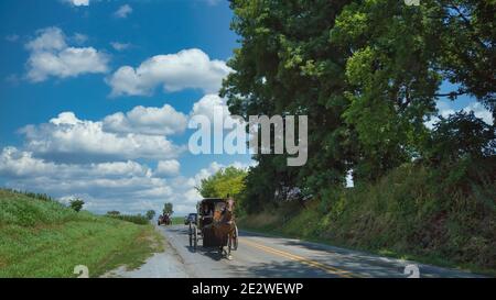 An Amish Horse and Buggy Being Followed by a Horse and Open Buggy on a Summer Day Stock Photo