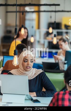 African muslim girl wearing hijab working on a laptop in a modern startup company. Stock Photo