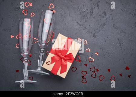 Valentine's day greeting card with champagne glasses and gift box with red ribbon on stone background. Top view with space for your greetings. Flat la Stock Photo