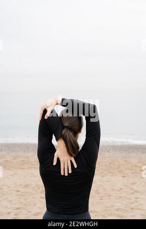 Young woman doing arm stretches as pre-exercise wain front of the sea Stock Photo