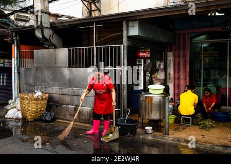 Woman in Pink Boots Cleans Street in Front of Talat Noi Shop in Bangko Stock Photo