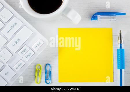 Yellow sheet of paper with space for text. Office accessories, computer keyboard, pen, coffee staples Stock Photo